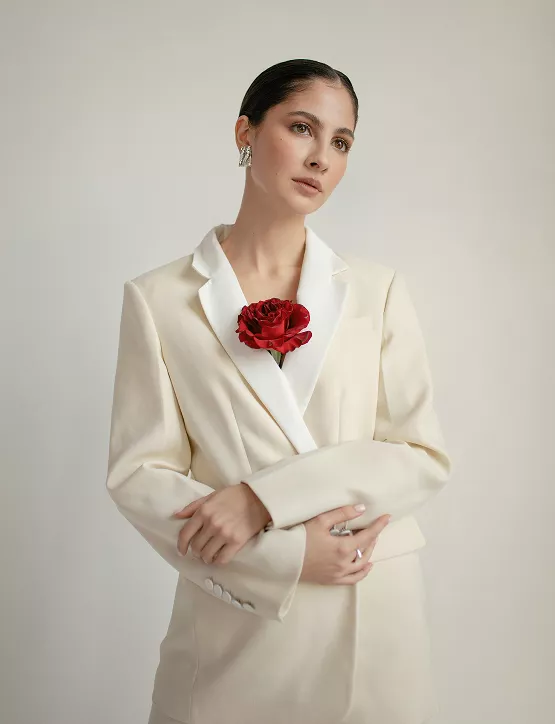  A woman in a white suit holds a red rose, exuding elegance and confidence.