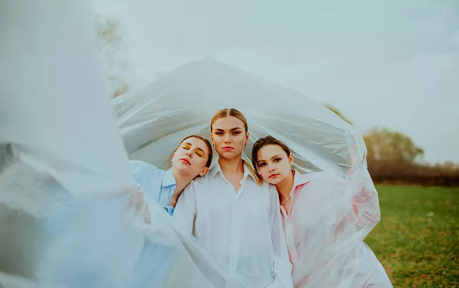 Three women wearing white shirts, with blue and pink accents, standing together and smiling